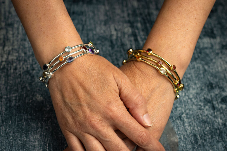 Silver and gold bangles set with multicoloured gemstones, worn on crossed wrists