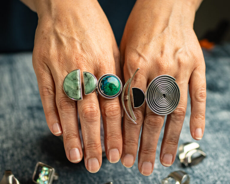Hands wearing five handmade silver rings set with green, turquoise and black stones