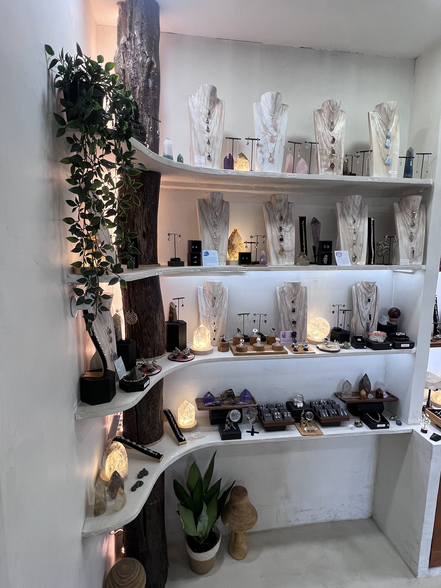 Sculpted white shelving inside the St Albans shop, hung with silver pendants and lit crystal points along a reclaimed timber beam.