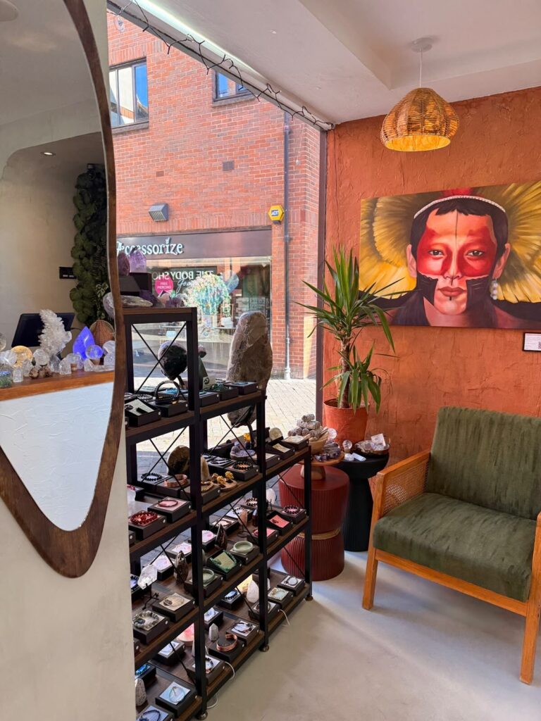 Inside the St Albans shop, a terracotta wall with a painted portrait, a green armchair, and a tall shelf unit of crystals and jewellery.