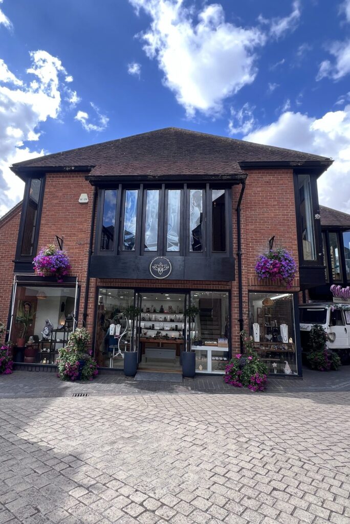 The Elements by Nature shopfront at The Maltings in St Albans, dark timber frontage with the gold lotus logo and hanging baskets of petunias.