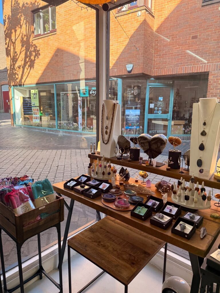The St Albans window display in afternoon light, agate slices, gemstone rings and pendants on wooden tables looking out onto The Maltings.