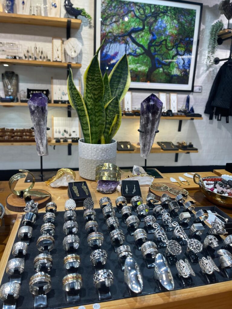 A tray of handmade silver rings with amethyst points behind, in the High Barnet shop